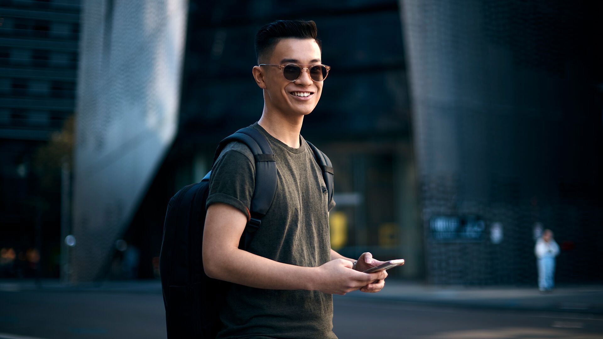 Student  wearing sunglasses and holding mobile phone standing outside UTS building 11