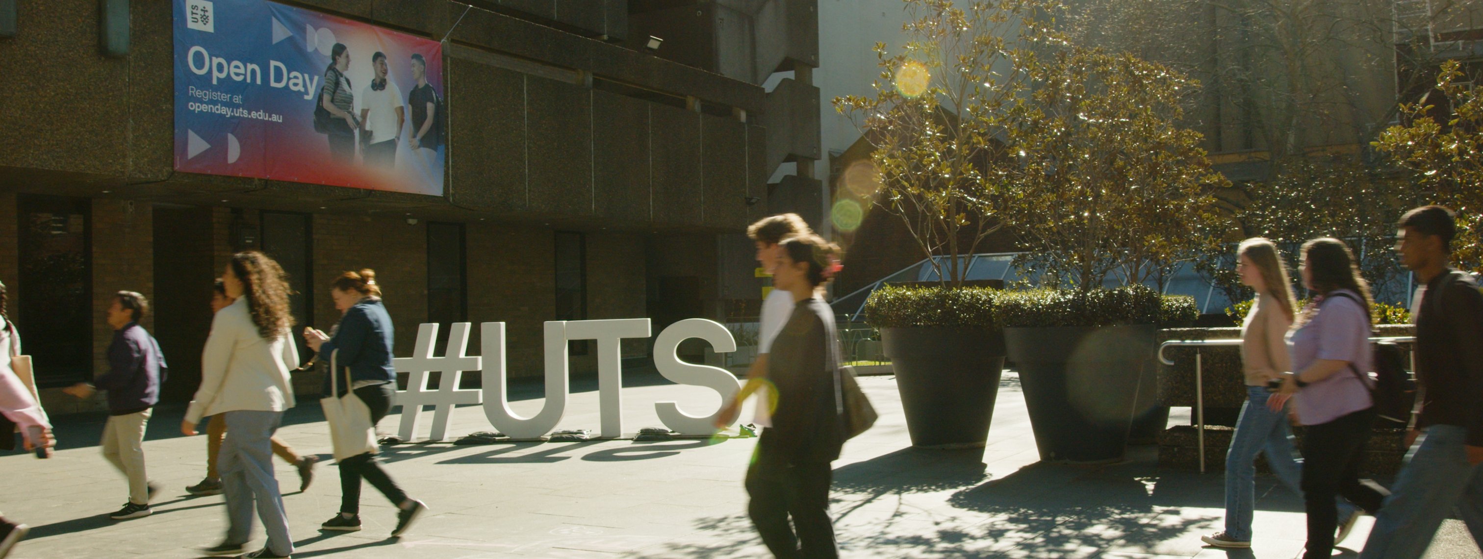 Students walking into the tower building. A large #UTS sign and Open Day banner is behind them.