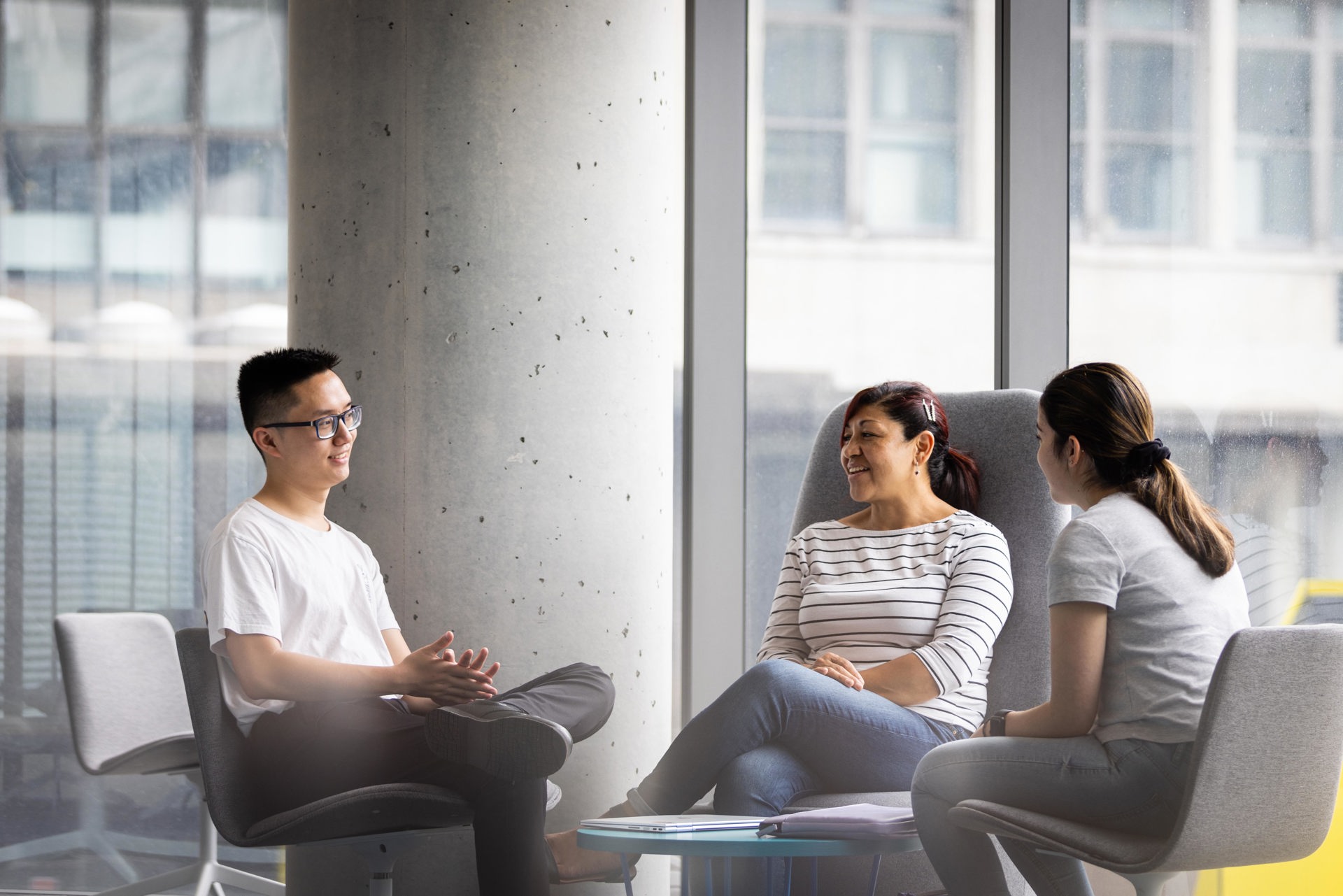 Three students sitting in chairs having a conversation.
