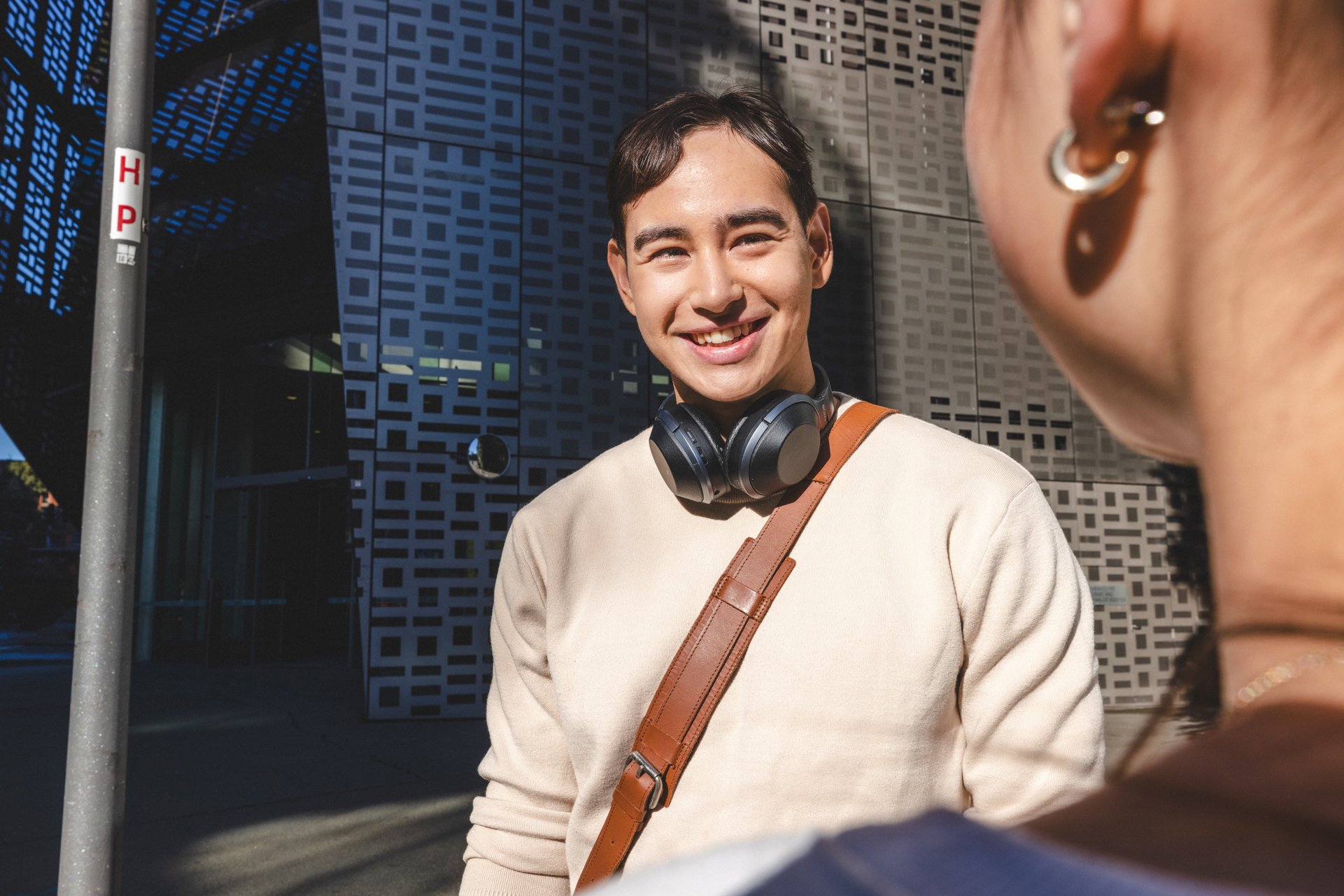 Male student standing outside UTS Engineering and IT building, smiling at another student he is talking to.