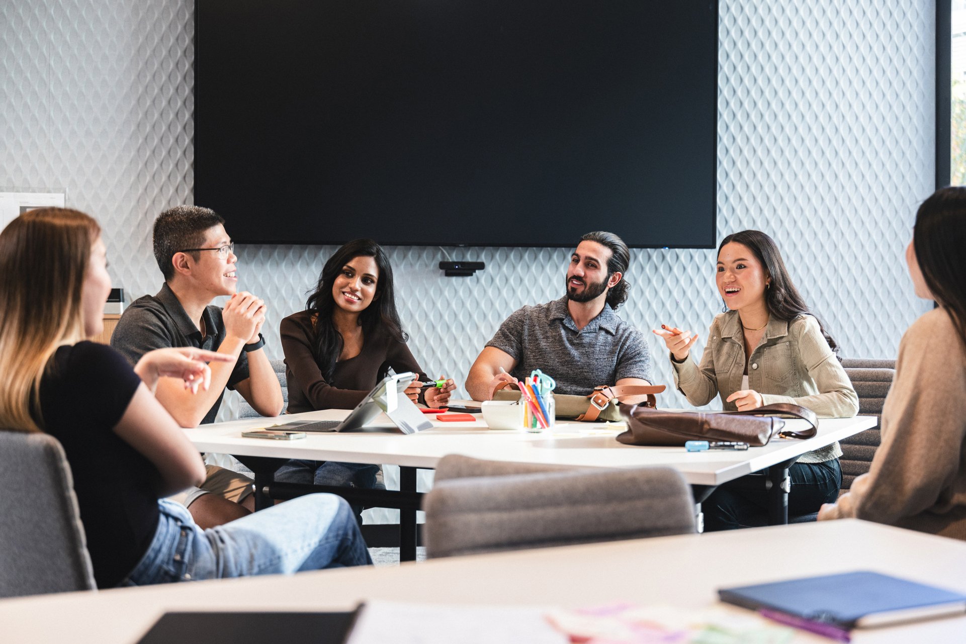Four female and two male students sitting around a table discussing ideas. Laptop and other stationery on table.