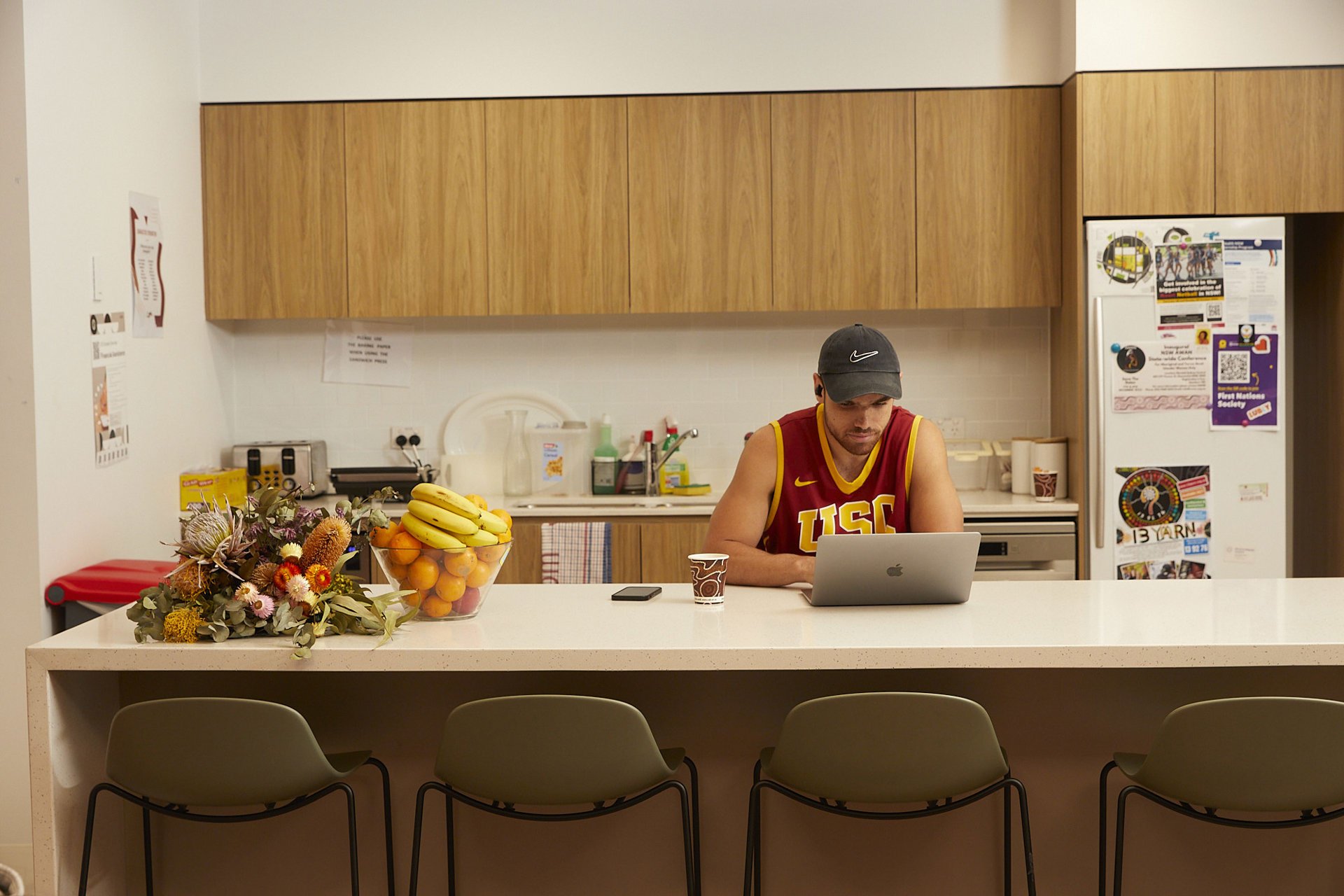 A man seated at a kitchen counter, focused on his laptop, surrounded by a cozy kitchen environment.