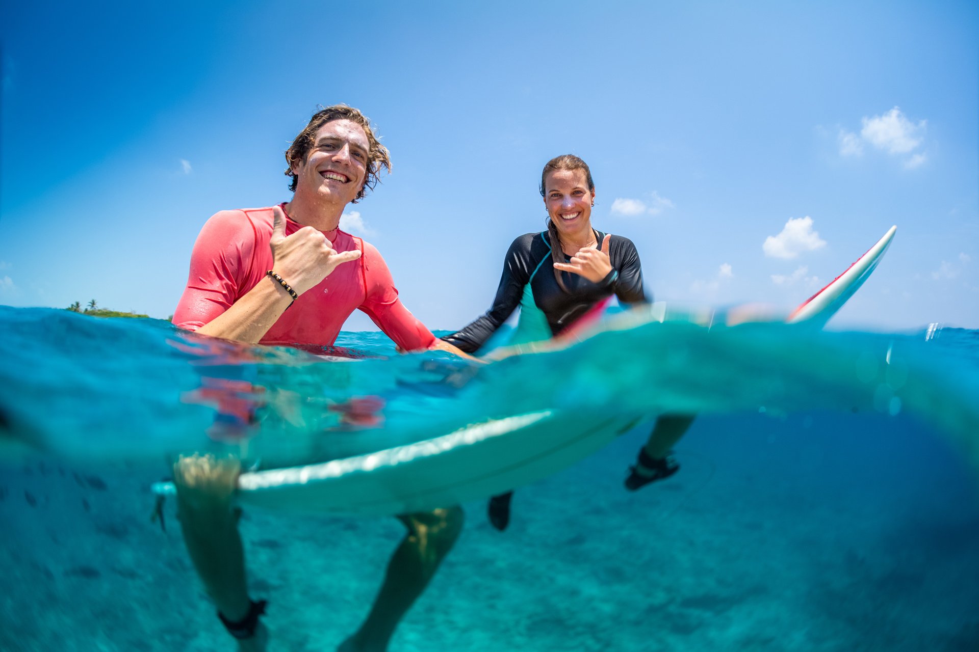 Young happy surfers man and woman sit on the surfboards in the water.